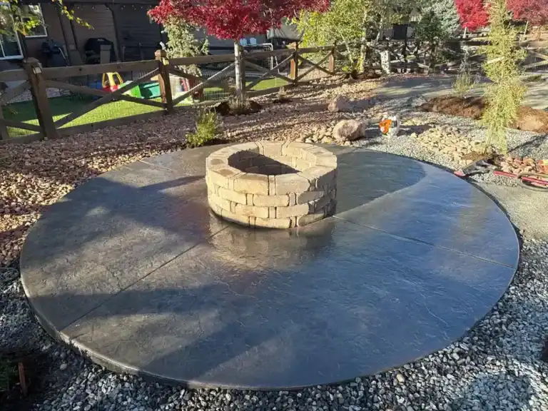 Circular stamped concrete patio surrounding a backyard fire pit in a landscaped yard in Colorado Springs.