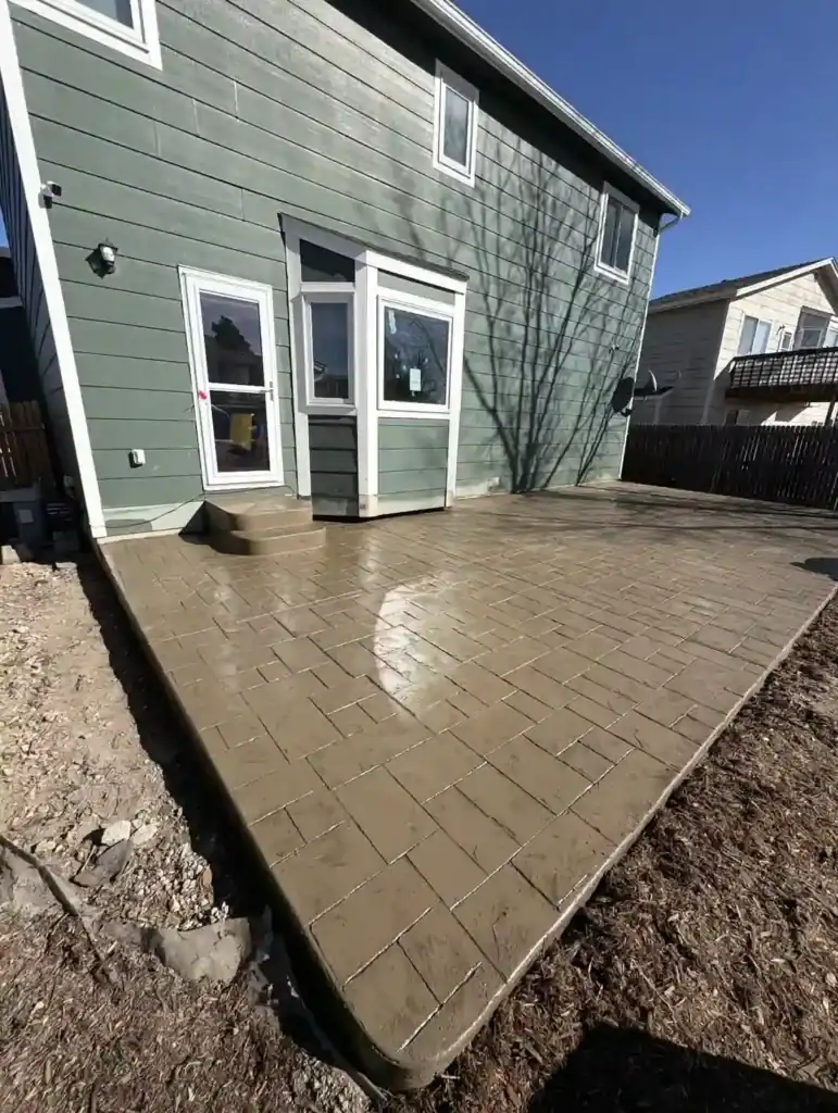 Freshly poured stamped concrete patio with a brick pattern behind a two-story home.