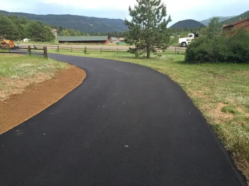 Newly paved asphalt driveway curving across a Colorado mountain property, with a road-base shoulder supporting the edge