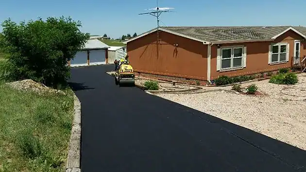 New asphalt driveway being rolled beside the old gravel at a rural Colorado home